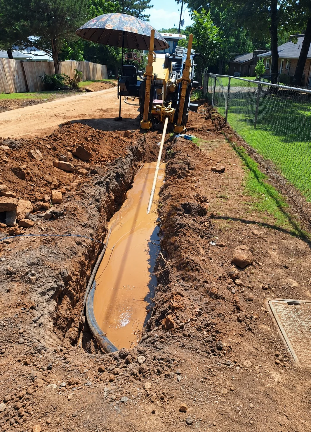 Directional drill rig running a bore with operator under sun umbrella